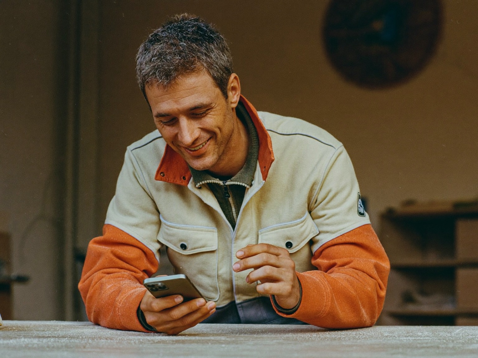 Handwerker in Arbeitsjacke schaut lächelnd auf sein Smartphone